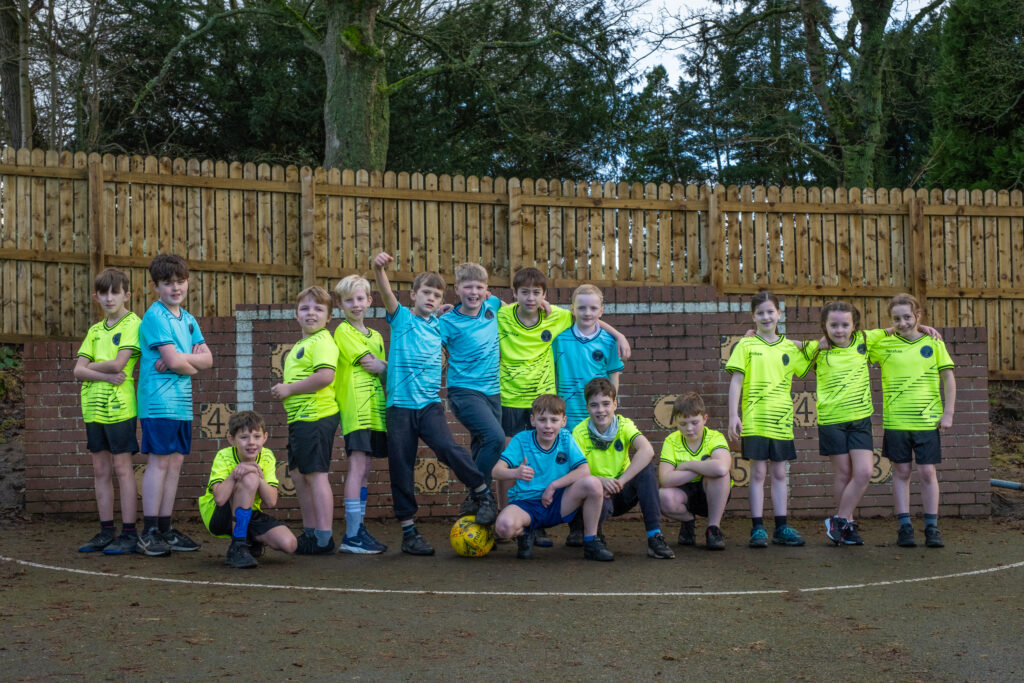 a group of children in football kits posing together in front of a football goal